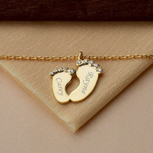 Gold personalized baby name necklace with delicate baby feet pendant displayed on a white background.