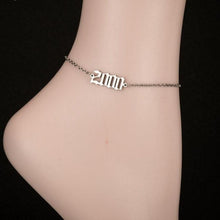Woman wearing a personalized birth year anklet with an Old English year charm.