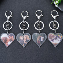 Four silver heart-shaped keychains with clear plastic inserts. Each keychain features a different photo: a couple kissing, a family of three, a couple with a child, and two cats.