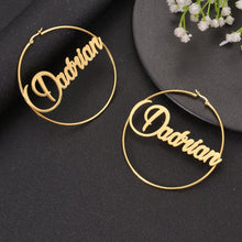 Large gold custom script name hoop earrings featuring retro cursive typography reading BabyDe across the center.