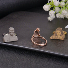 Three silver rings with engraved images of people. The rings are on a black surface.