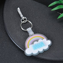 Pastel rainbow cloud acrylic keychain featuring custom blue glitter block text MAMA with silver metal keyring hardware.