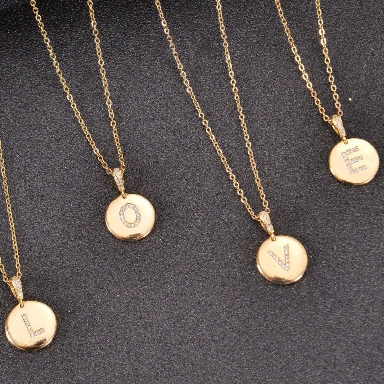 Four gold initial disc necklaces spelling "LOVE"