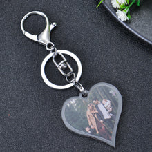 A silver heart-shaped keychain with a photo of a family of four in a forest setting. The keychain has a silver ring and a silver clasp.