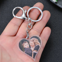 A silver heart-shaped keychain with a photo of a woman and a child inside. The keychain has a silver split ring and a silver lobster clasp.