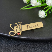 Gold custom nurse pin featuring stethoscope outline with red crystal, syringe cutout, and custom engraved script name Franek.