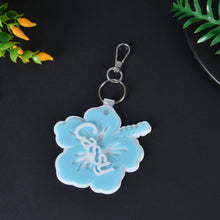 Light blue acrylic floral keyring customized with white overlay script name Cassy and hibiscus stamen detail.