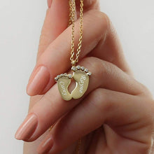 Close-up of a personalized baby feet pendant showing custom engraved names on the tiny footprint charms.