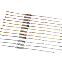 Grouping of gold, rose gold, and silver name bar bracelets laid parallel on white surface.