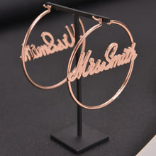 Medium rose gold custom script name hoop earrings featuring modern cursive nameplate Mrs. Smith centered inside.