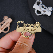 Close-up of custom engraved name on gold stethoscope-shaped badge