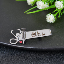 Silver personalized medical brooch featuring stethoscope with red gem, syringe detail, and custom engraved cursive name Olivia.